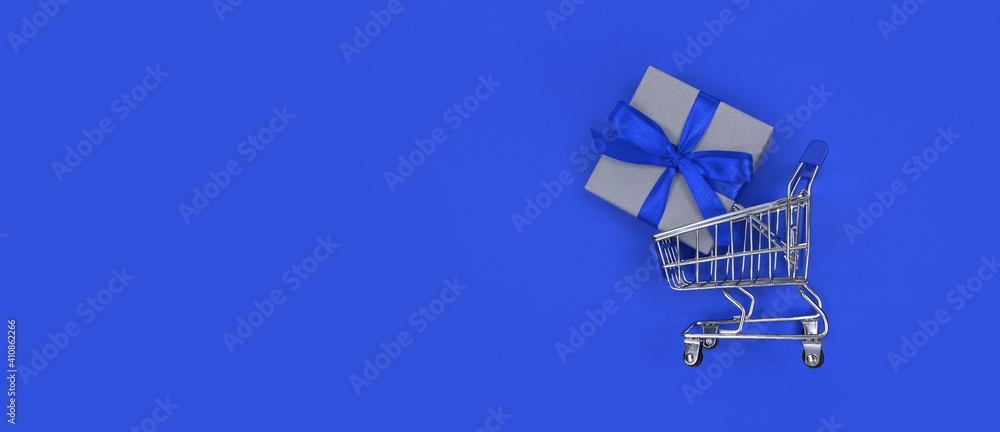 Supermarket trolley and gift box on blue background with copy space. Shopping concept. Supermarket trolley and gift box on blue background with copy space. Shopping concept.