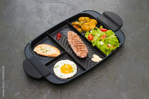Breakfast, fried steak or cutlet, salad with tomato and green vegetables, toast, potatoes, egg on black plate. The concept of a healthy diet, diet, menu, high-grade lunch
