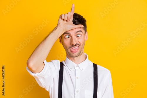Photo portrait of comic silly ridiculous man showing looser sign abusing fooling grimacing isolated on bright yellow color background photo