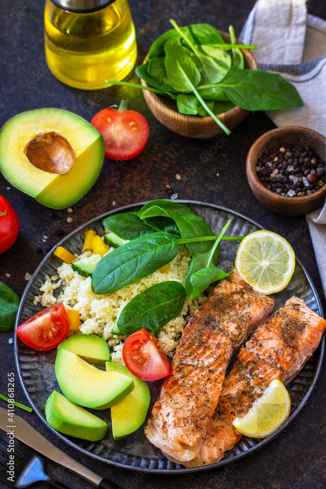 Grilled salmon fillet with couscous, salad fresh vegetables and avocado on dark background. Grilled salmon fillet with couscous, salad fresh vegetables and avocado on dark background.