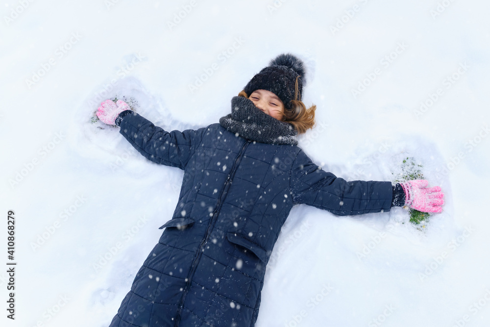 child girl lies on the snow and makes angel wings, bright sunlight and shadows on the snow, beautiful nature