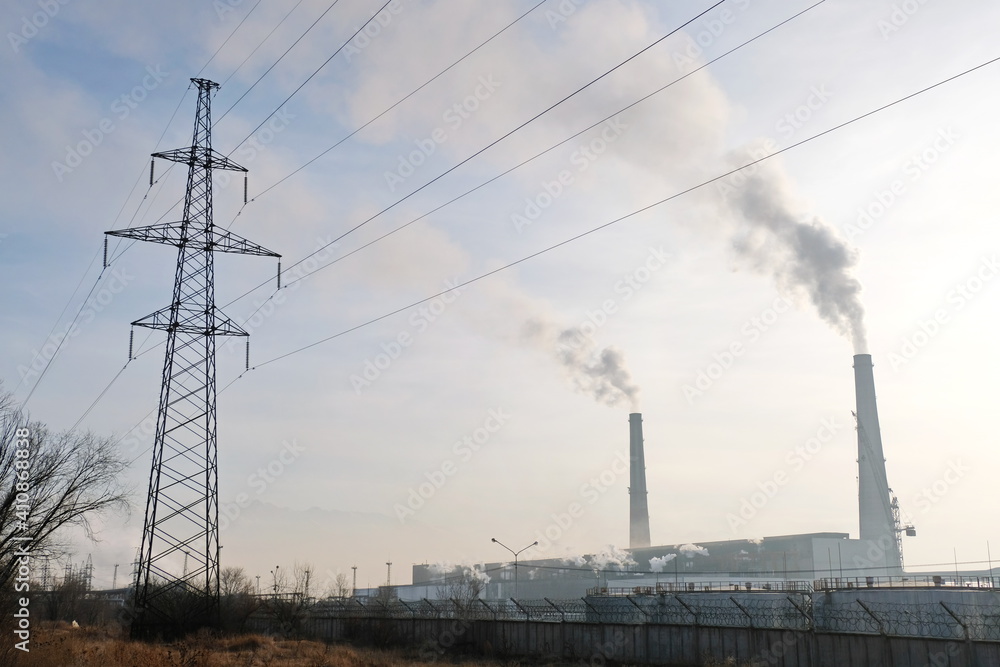 Almaty, Kazakhstan - 02.04.2021 : Power lines on the background of the building of the main heating plant with smoking pipes Almaty, Kazakhstan - 02.04.2021 : Power lines on the background of the building of the main heating plant with smoking pipes