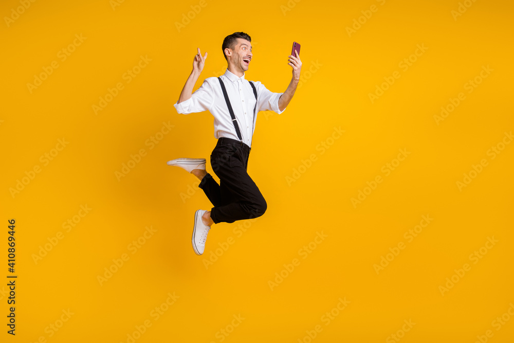 Full length body size photo of jumping man taking selfie showing v-sign gesture isolated on vibrant yellow color background