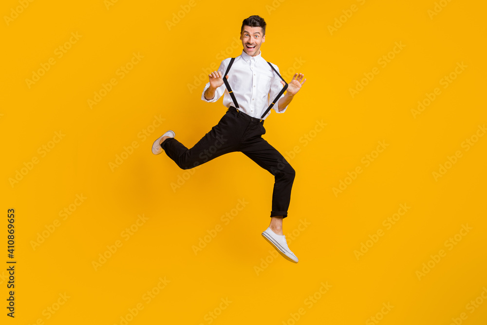 Full body photo of cheerful person hands playing with suspenders jump high isolated on yellow color background