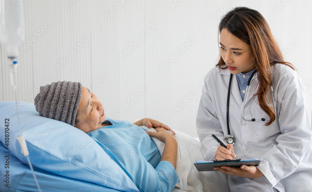 Young and beautiful doctor asking and note for diagnosis with Older Asian woman patient covered the head with clothes effect from chemo treatment in cancer cure process Young and beautiful doctor asking and note for diagnosis with Older Asian woman patient covered the head with clothes effect from chemo treatment in cancer cure process