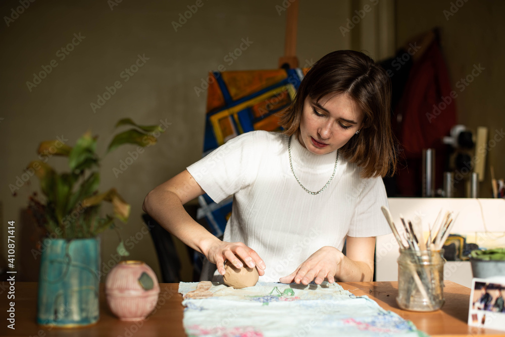 young artist moulding raw clay in art studio. Girl molds from clay sculpture in the artist's studio. Business woman at her pottery store