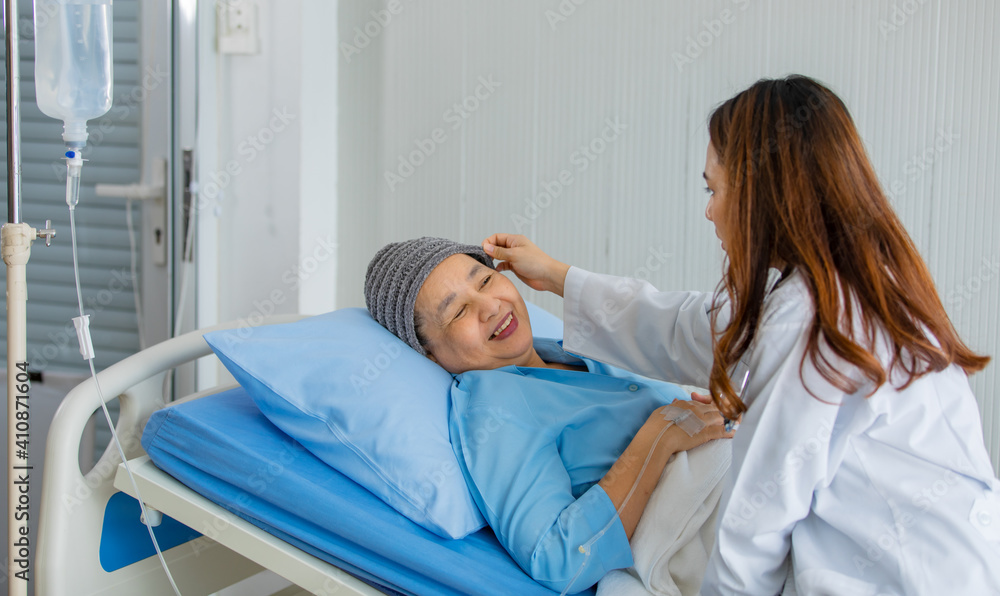 Fototapeta premium Older Asian woman patient covered the head with clothes effect from chemo treatment in cancer cure process talking to a female doctor