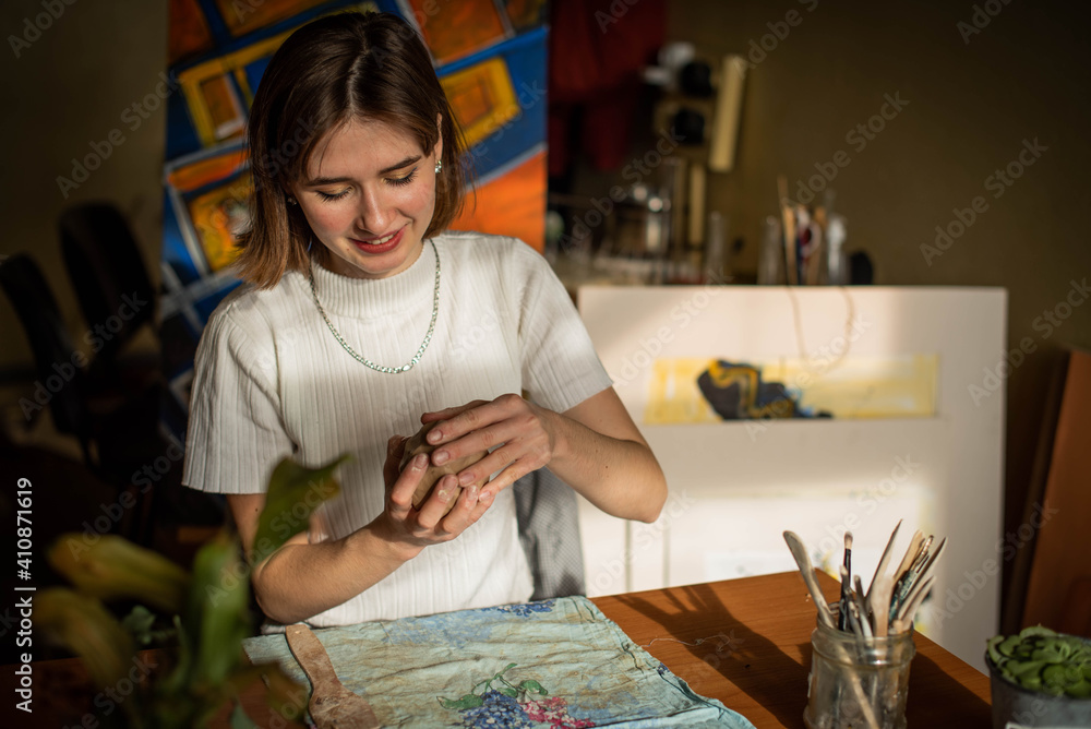 young artist moulding raw clay in art studio. Girl molds from clay sculpture in the artist's studio. Business woman at her pottery store