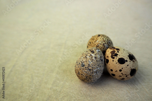 three raw quail eggs lie side by side on a light beige background . healthy eating