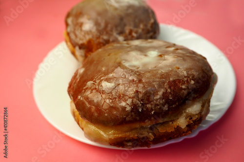 close up two donuts in sugar glaze lie in a white round plate on a pink background side view