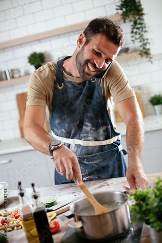  Happy man baking in the kitchen. Man talking to the phone while making fresh pasta.