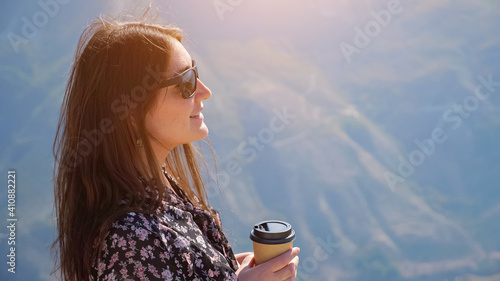 Foto Brunette woman with stylish sunglasses in color dress drinks coffee enjoying won