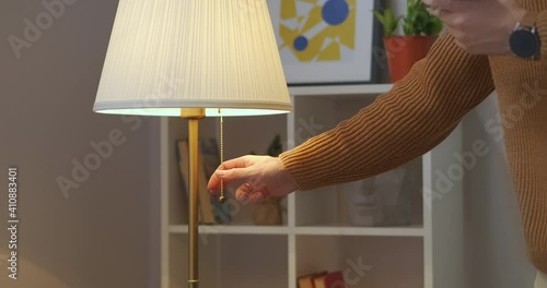 man is turning off floor lamp in living room or bedroom at evening, interior of modern apartment