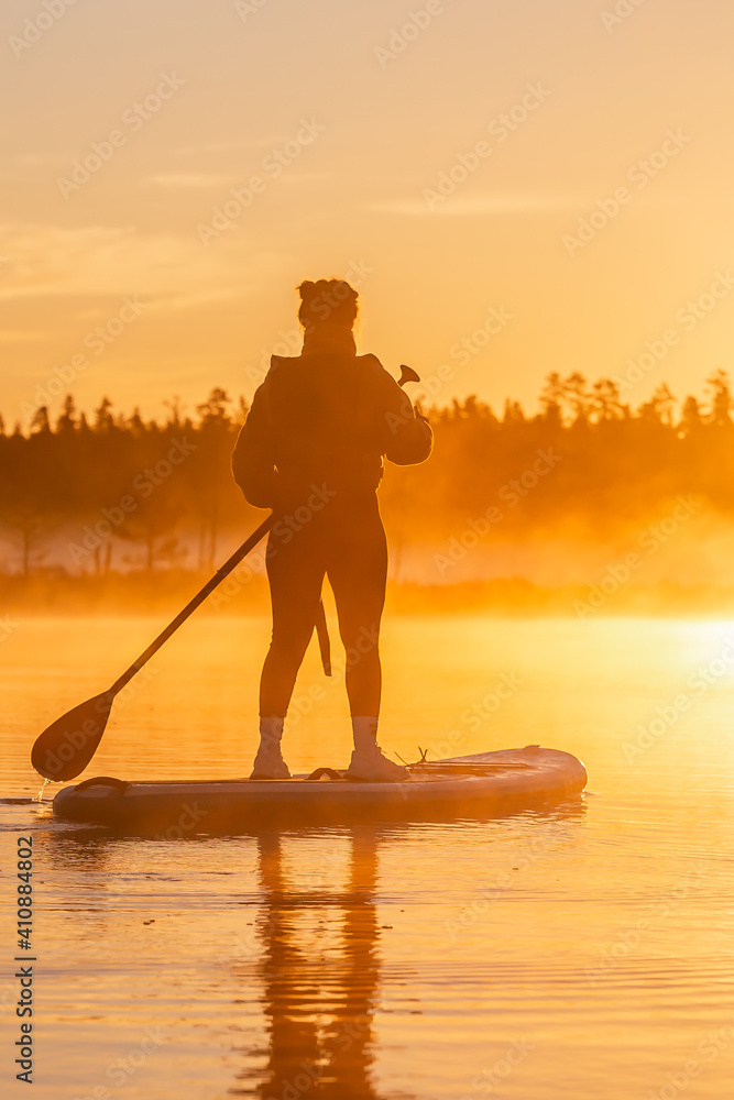 Silhouette of Young asian woman doing SUP stand up paddle boarding at sunrise in lake. Early summer morning activity
