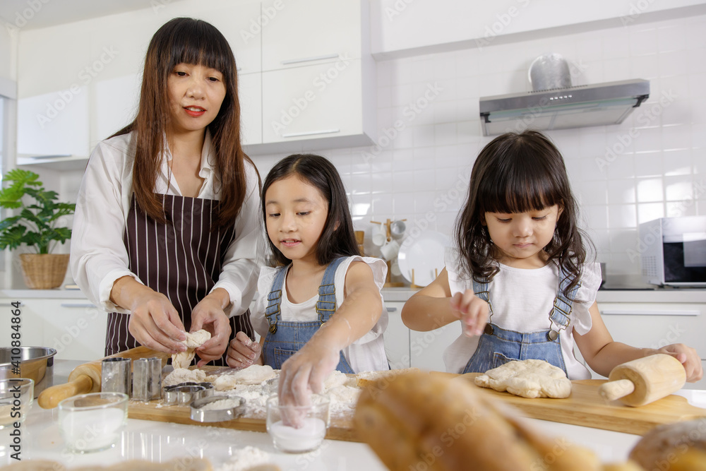 Family group photo of 30s mom teaching and educate two little girls, 3 years and 7 years old, how to make bread and bakery. They are learning and playing with flour in a modern kitchen