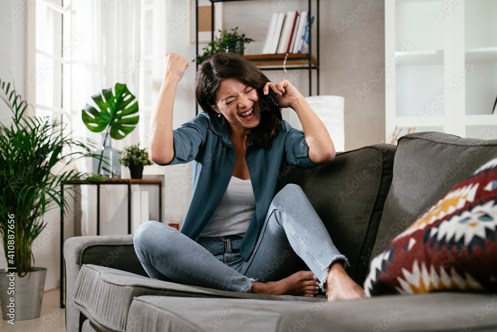 Happy young woman talking to the phone at home. Excited woman enjoying in the living room..