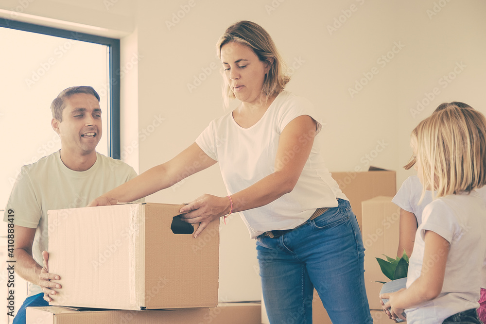 Beautiful blonde mother putting carton box on another one. Happy family with two daughters moving together in big new apartment or house. Mortgage, relocation and moving day concept Beautiful blonde mother putting carton box on another one. Happy family with two daughters moving together in big new apartment or house. Mortgage, relocation and moving day concept
