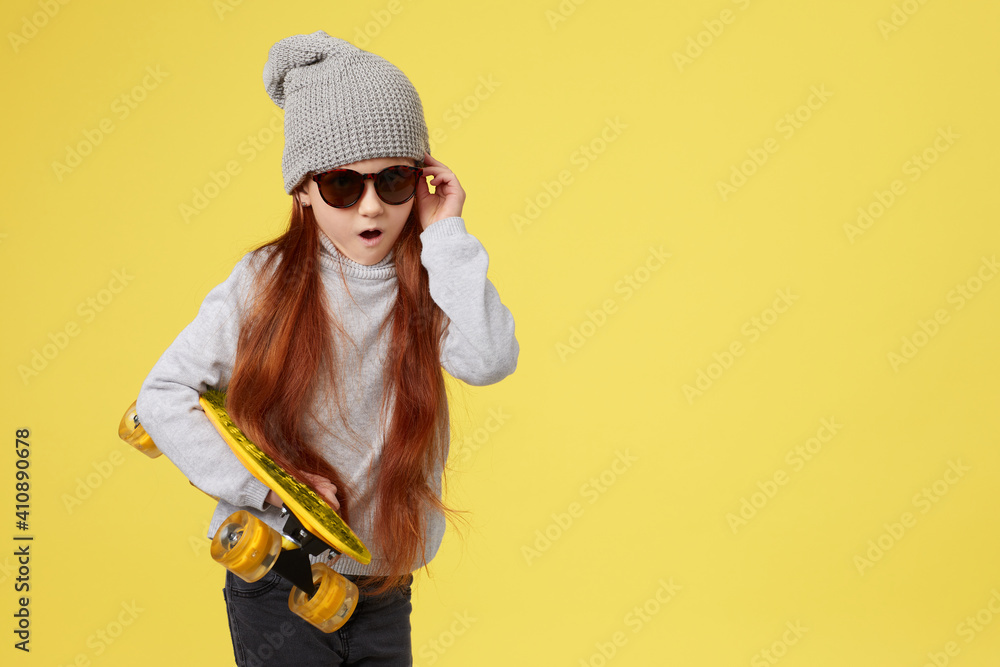 surprised little child girl in hat with yellow skateboard wearing hipster casual clothes over yellow background. copy space for text surprised little child girl in hat with yellow skateboard wearing hipster casual clothes over yellow background. copy space for text