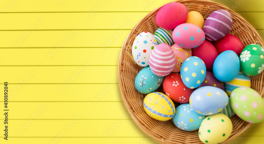 Fototapeta premium easter, holidays and tradition concept - close up of colored eggs in basket over yellow wooden boards background