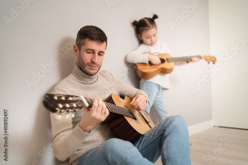Dad plays the guitar with his daughter. The child learns to play a musical instrument with a tutor. Musical duet of a father with a child