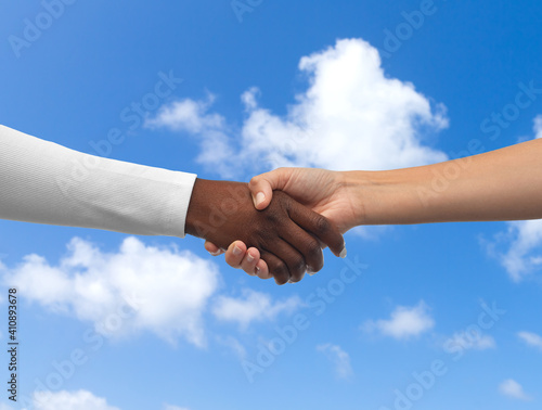 communication, cooperation and people concept - handshake of black and white hands over blue sky and clouds background © Syda Productions