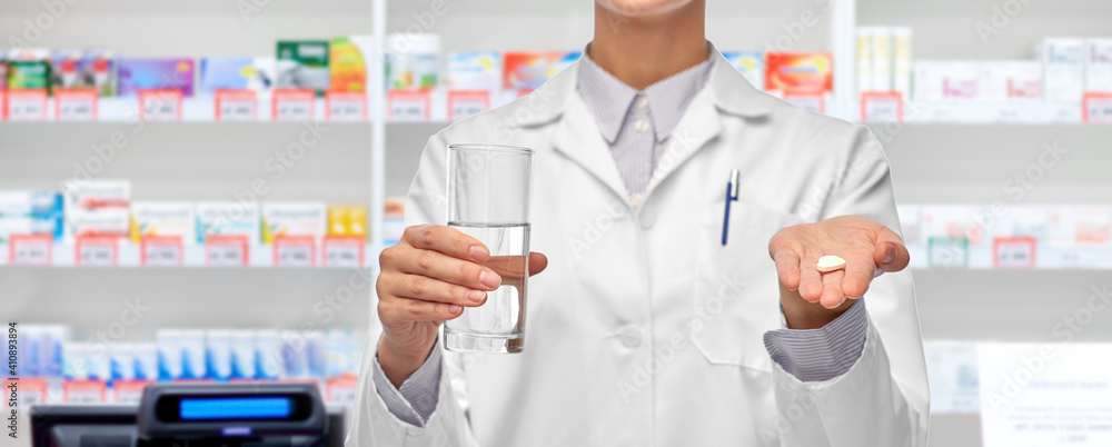 medicine, profession and healthcare concept - close up of female doctor or pharmacist with pill and glass of water over pharmacy on background