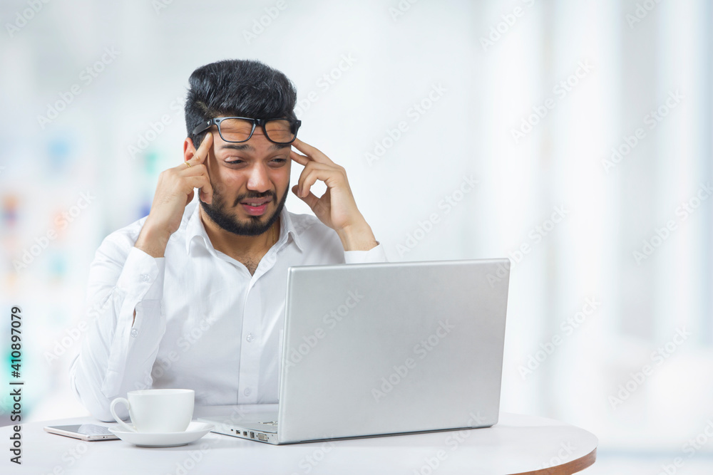 Young man holding his head in frustration due to workload in office. 	
