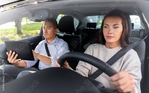 driver courses and people concept - woman and driving school instructor with tablet computer in car