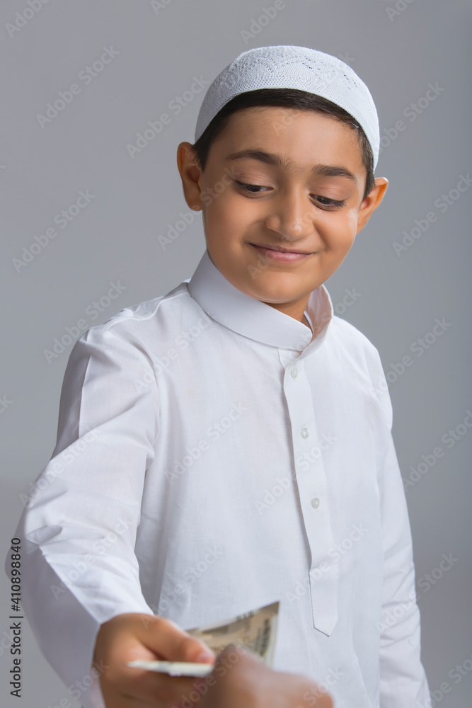 Young Muslim boy wearing cap smiling and giving away money Young Muslim boy wearing cap smiling and giving away money