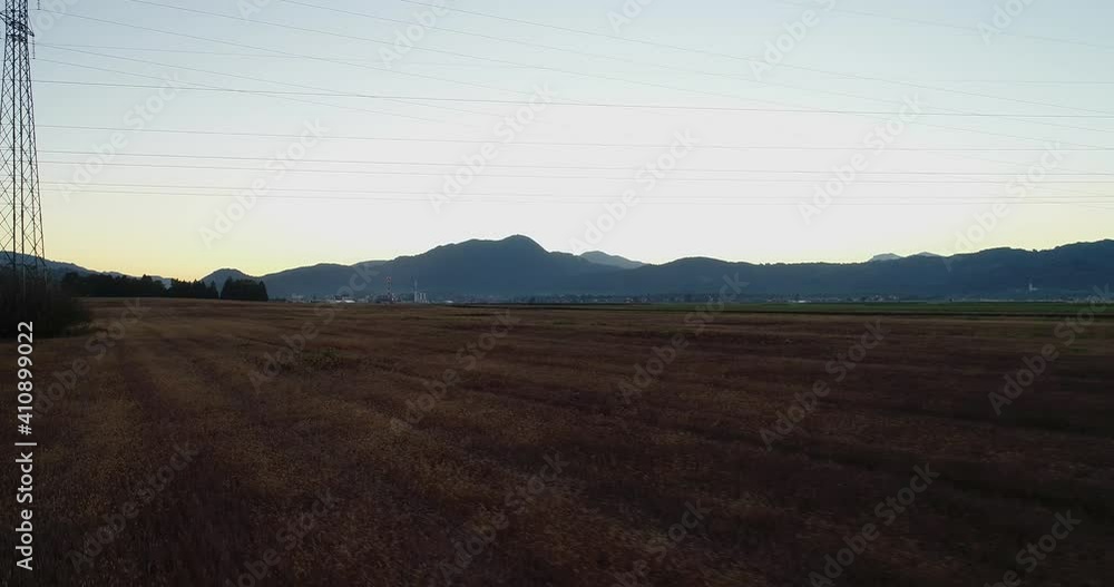 Low flying drone over agriculture farmland farming fields and mountains in the distance. Agronomy flatland in large basin, Slovenia. Electric pylon and wires on the field. Backward moving Low flying drone over agriculture farmland farming fields and mountains in the distance. Agronomy flatland in large basin, Slovenia. Electric pylon and wires on the field. Backward moving