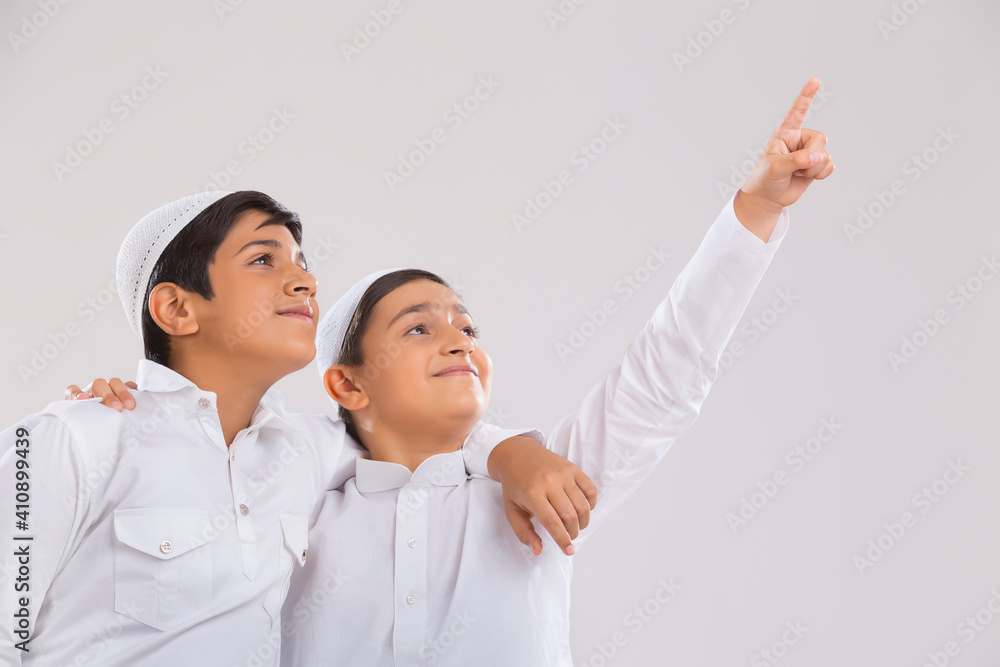 Young Muslim boys wearing cap looking away, smiling and pointing Young Muslim boys wearing cap looking away, smiling and pointing