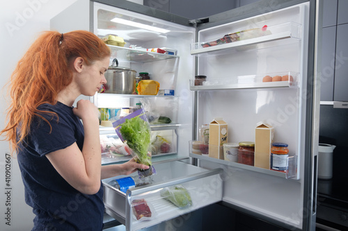 Woman standing at the open refrigerator with fruits, vegetables and healthy food