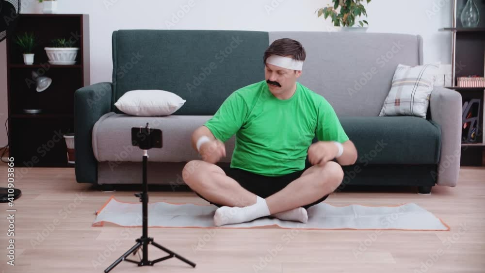 A funny male athlete sits on the floor looking at a smartphone and listens to what they say to him on the video and points to his biceps. Beauty and sports concept. A funny male athlete sits on the floor looking at a smartphone and listens to what they say to him on the video and points to his biceps. Beauty and sports concept.
