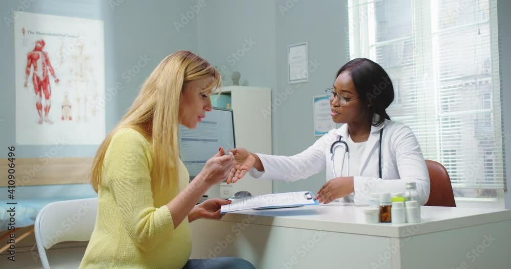 Medium shot of pregnant woman visit african american gynecologist at hospital or medical clinic. Doctor giving documents, papers to female for signing. Pregnancy and maternity healthcare concept. Medium shot of pregnant woman visit african american gynecologist at hospital or medical clinic. Doctor giving documents, papers to female for signing. Pregnancy and maternity healthcare concept.