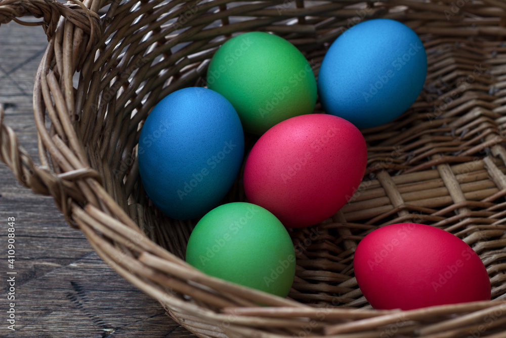 Colored easter eggs in wicker basket on wooden surface Colored easter eggs in wicker basket on wooden surface