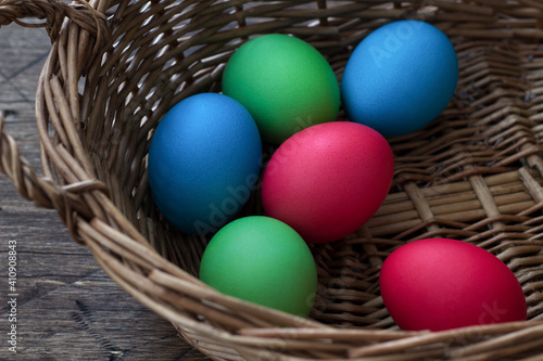 Colored easter eggs in wicker basket on wooden surface