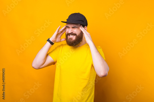 Photo of young man having headache over yellow background.