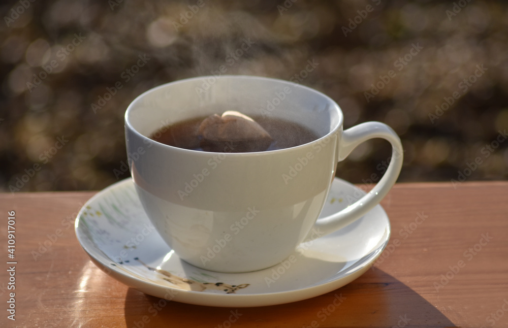 Hot tea cup on a frosty winter day put on wooden table with background of front garden in morning. Hot tea cup on a frosty winter day put on wooden table with background of front garden in morning.