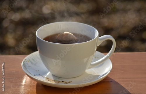 Hot tea cup on a frosty winter day put on wooden table with background of front garden in morning.