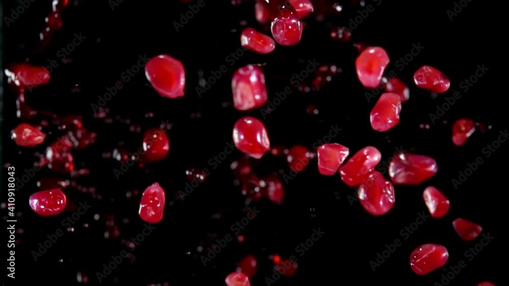 Fresh pomegranate grains are bouncing with splashes of red juice on the black background in slow motion Fresh pomegranate grains are bouncing with splashes of red juice on the black background in slow motion