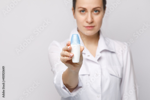 Young female doctor wearing medical coat holding bottle of antibacterial soap  smiling nurse on white isolated background  hospital worker