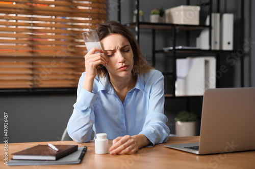Woman holding glass of medicine for hangover in office