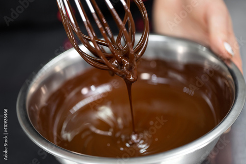 Obraz na płótnie Pastry chef whips melted chocolate in a bowl with a metal wire whisk close up