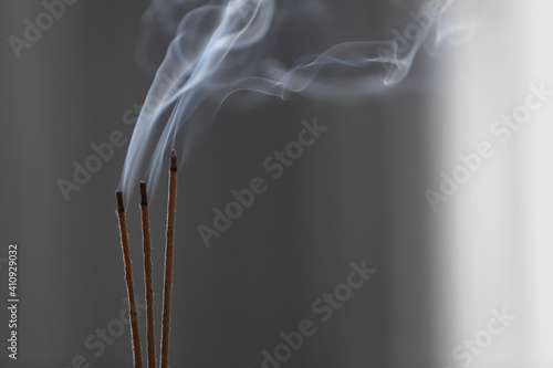 Incense sticks smoldering on blurred background, closeup. Space for text