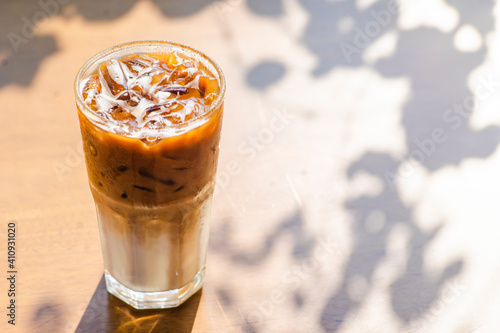 Ice coffee on a wood table with cream being poured into it showing the texture and refreshing look of the drink
