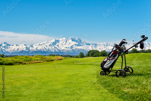 Golf cart with bag and golf clubs at the edge of the fairway of a golf course. In the background the Alps, the Monte Rosa chain, seen from the Italian side.