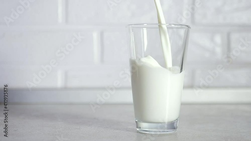 Slow motion shot of pouring, splashing fresh milk into a transparent glass against white background. Dairy product concept. Filling glass with milk close up