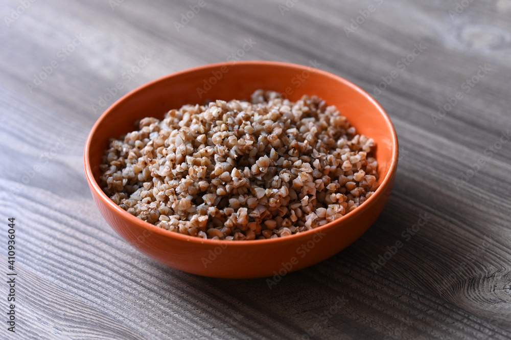 Orange ceramic plate with buckwheat porridge on a wooden table. Image with selective focus. Orange ceramic plate with buckwheat porridge on a wooden table. Image with selective focus.