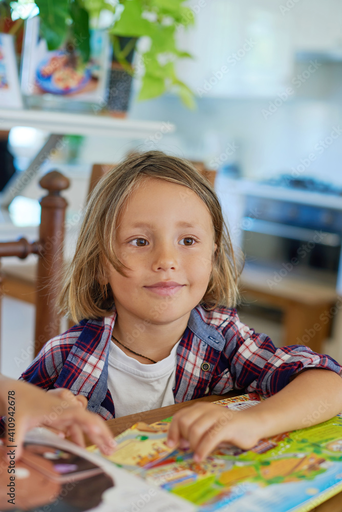 Portrait of joyful little boy which poses sitting at table with books and looks away in living room. Portrait of joyful little boy which poses sitting at table with books and looks away in living room.