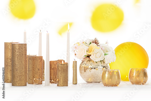 Table décorée de bougies dorées et blanches et de fleurs pour un repas de fête avec ballons jaunes qui tombent en arrière plan. photo
